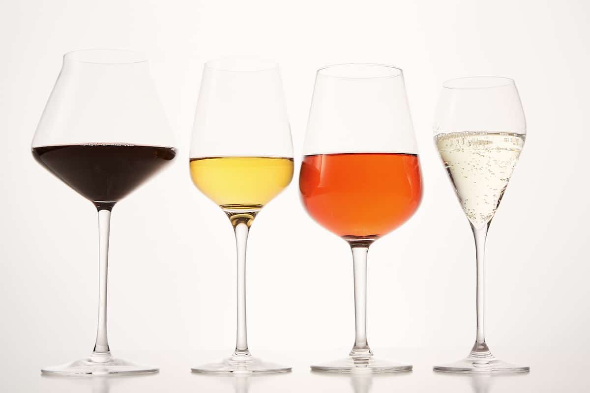 Bowls of wineglasses on stems filled with different types of wine. Pink, white, red, sparkling alcoholic beverages are in stemware for tasting, evaluation. Drinks for party, holiday event. Closeup.