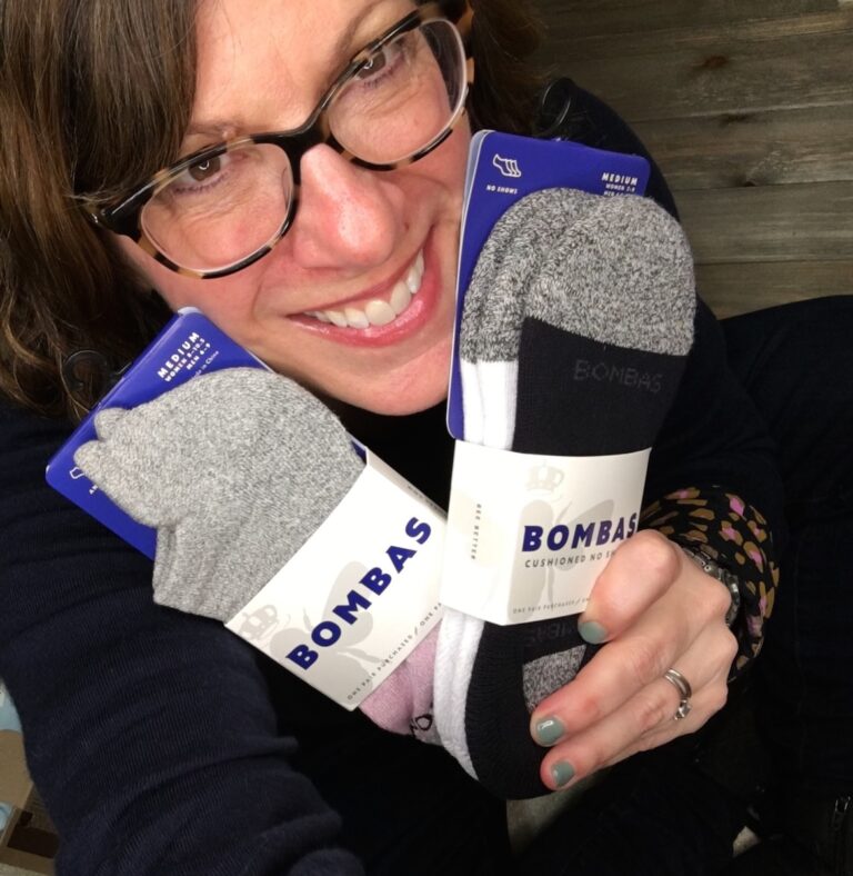 Woman with glasses holding up two pairs of Bombas socks.