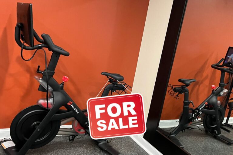 Peloton bike with for sale sign on it in front of mirror.
